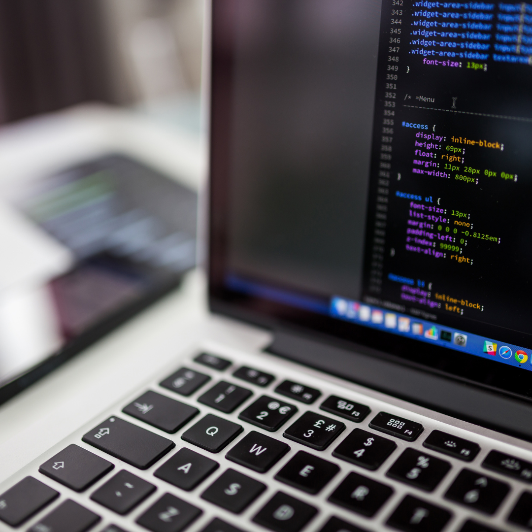 A close-up view of a laptop displaying code on the screen, with a blurred background of a smartphone and workspace.