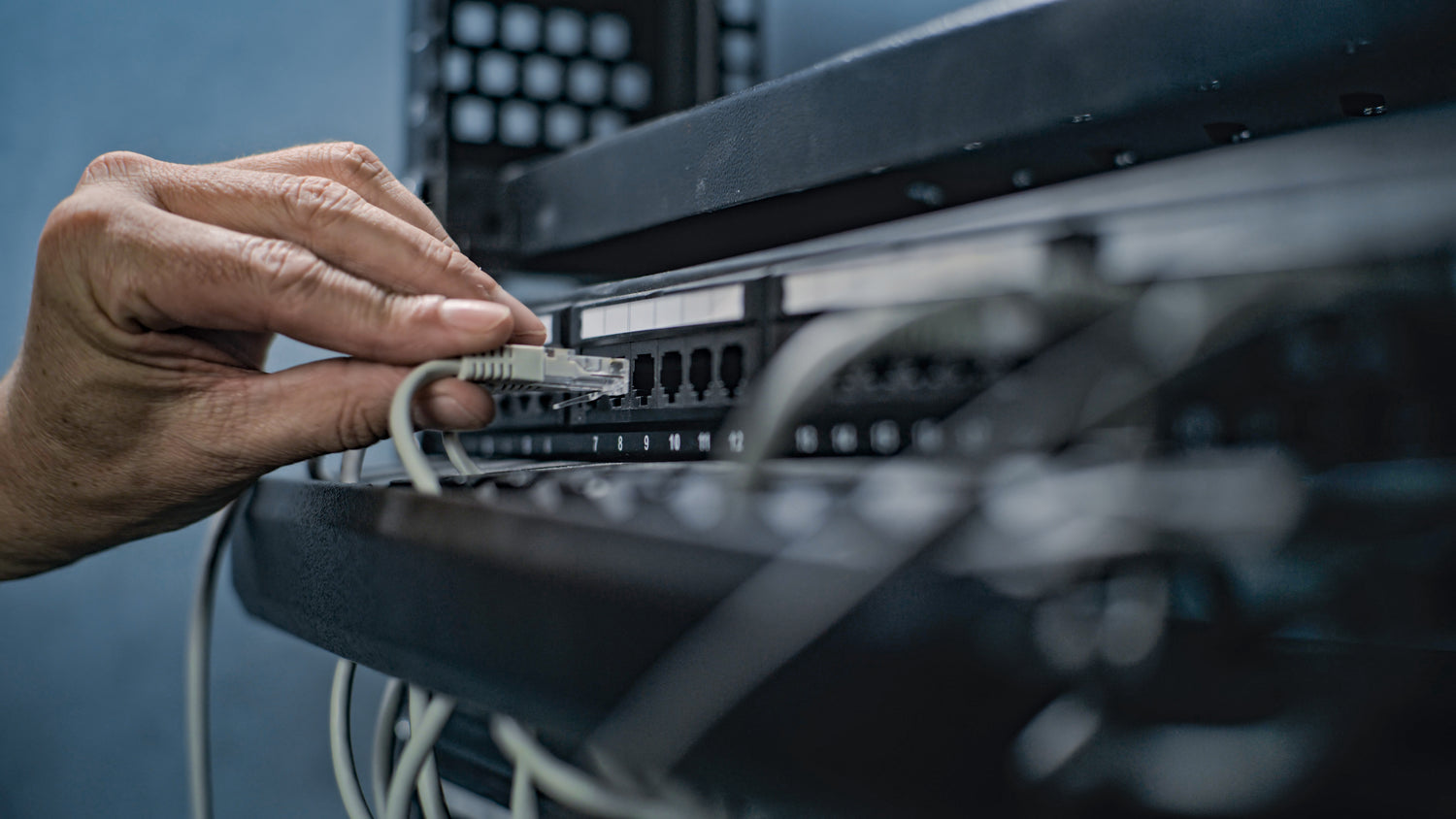 A hand connecting an Ethernet cable to a network switch, illustrating network infrastructure management.