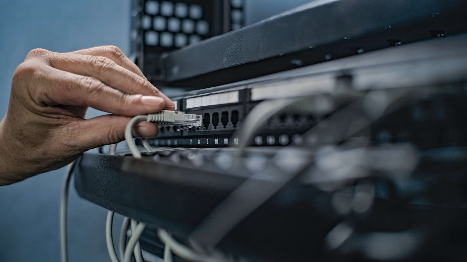 A hand connecting an Ethernet cable to a network switch, illustrating network infrastructure management.