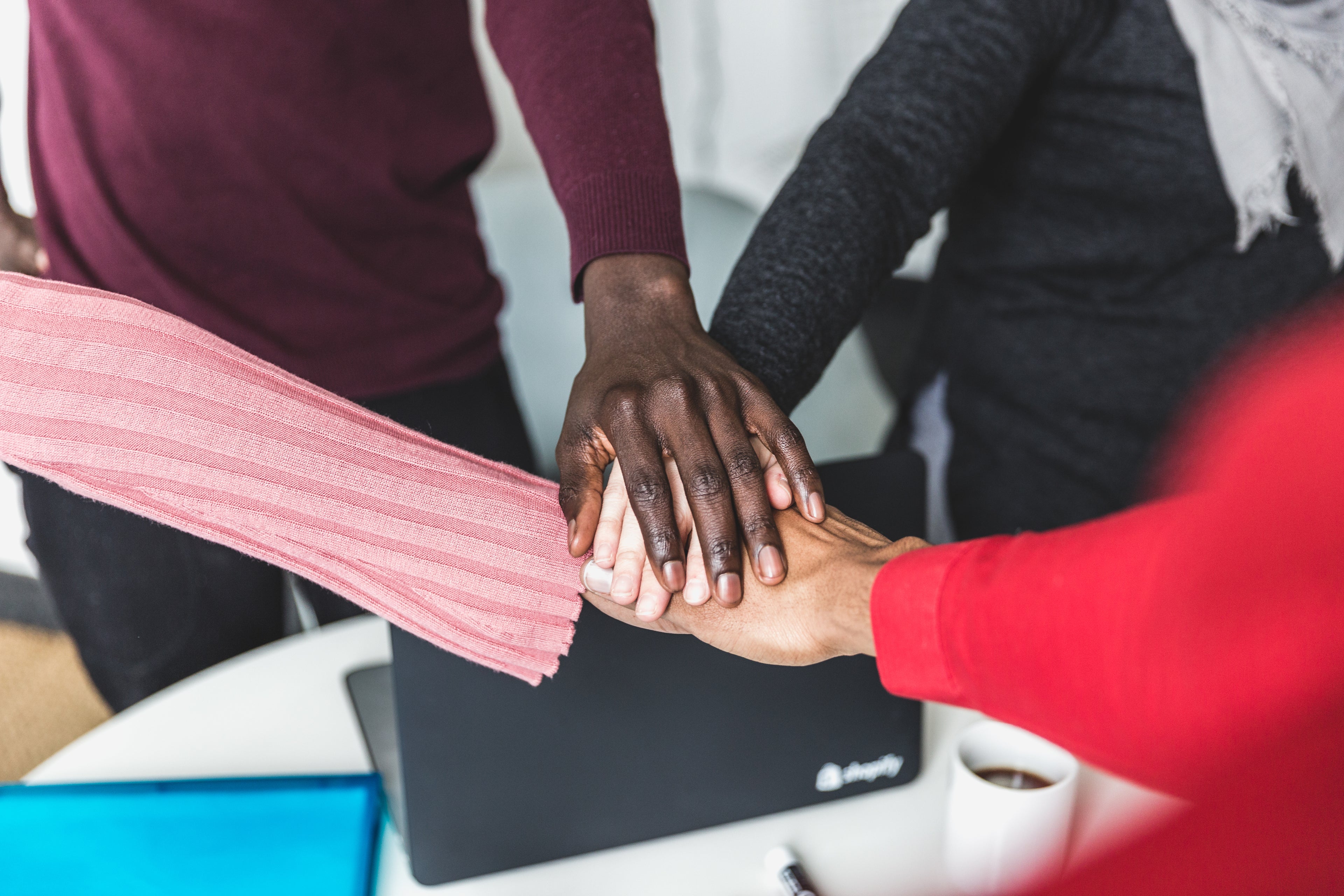Teamwork at Aptimized: diverse hands united in collaboration over a desk, symbolizing innovation, inclusivity, and success.