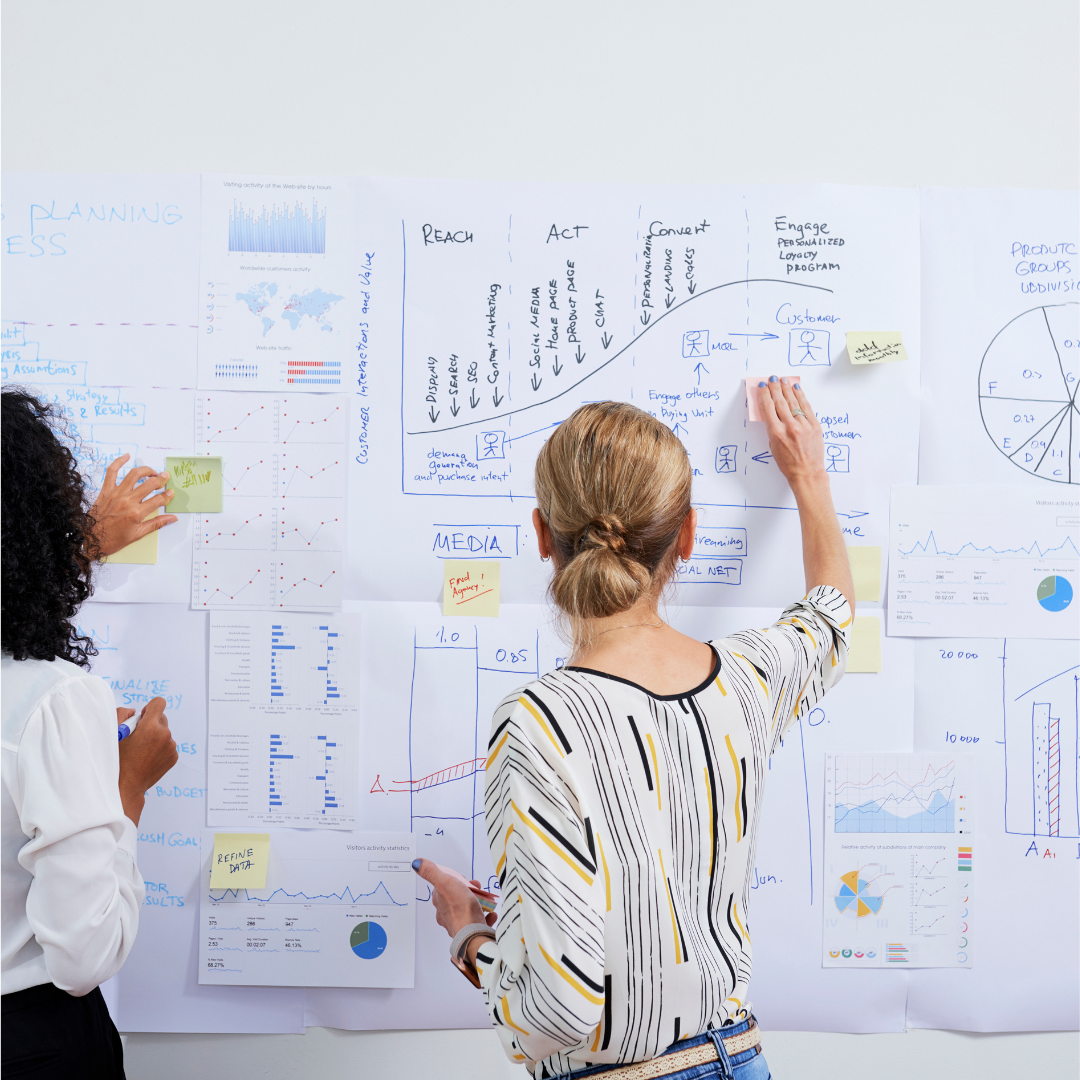 Team collaboration in a workspace, analyzing charts and diagrams on a whiteboard for strategic planning.