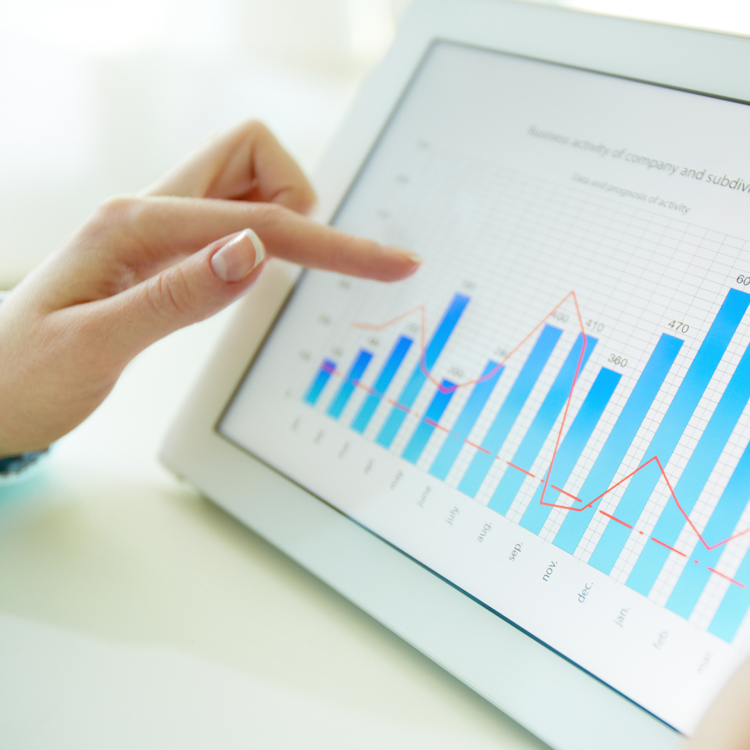 A hand points to a tablet displaying a bar graph and line chart, illustrating company performance metrics and trends.