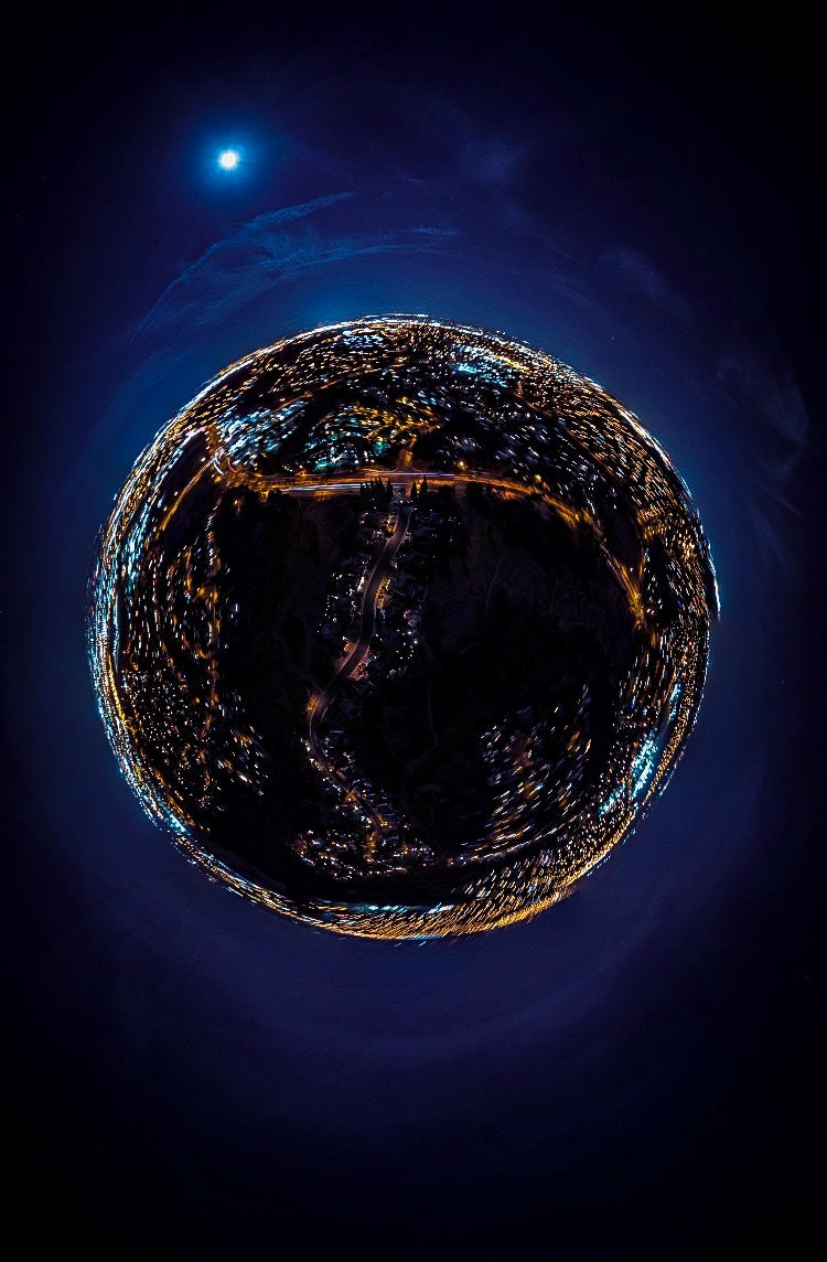 Spherical night view of a city with glowing lights and a moonlit sky, captured using a fisheye or "tiny planet" effect.